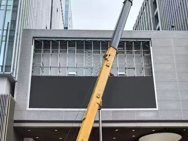 A detailed view of an orange truck crane in Rwanda lifting a complete die-cast aluminum LED cabinet, weighing only, towards the single-pole framework.