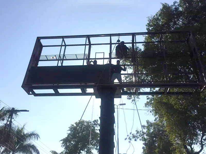 Close-up of construction workers on a single-pole steel framework in Rwanda, preparing to lift the die-cast aluminum LED display cabinets. The frame highlights the minimal structural requirements needed for these lightweight screens.
